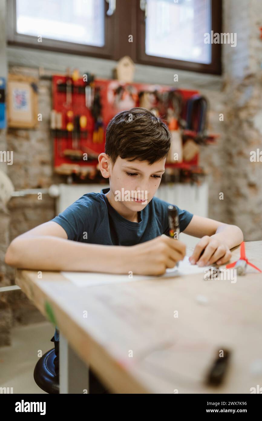 Studente maschio che lavora al progetto di robotica mentre è seduto a tavola in officina Foto Stock