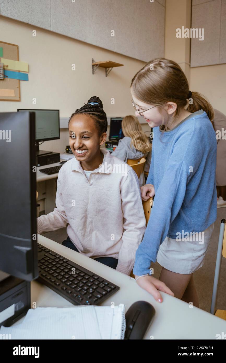 Felici ragazze multirazziali che si divertono in classe di computer a scuola Foto Stock