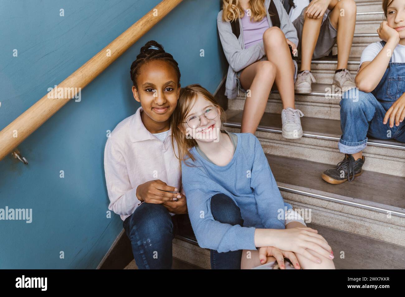 Ritratto di amiche multirazziali sorridenti sedute su una scala nell'edificio scolastico Foto Stock