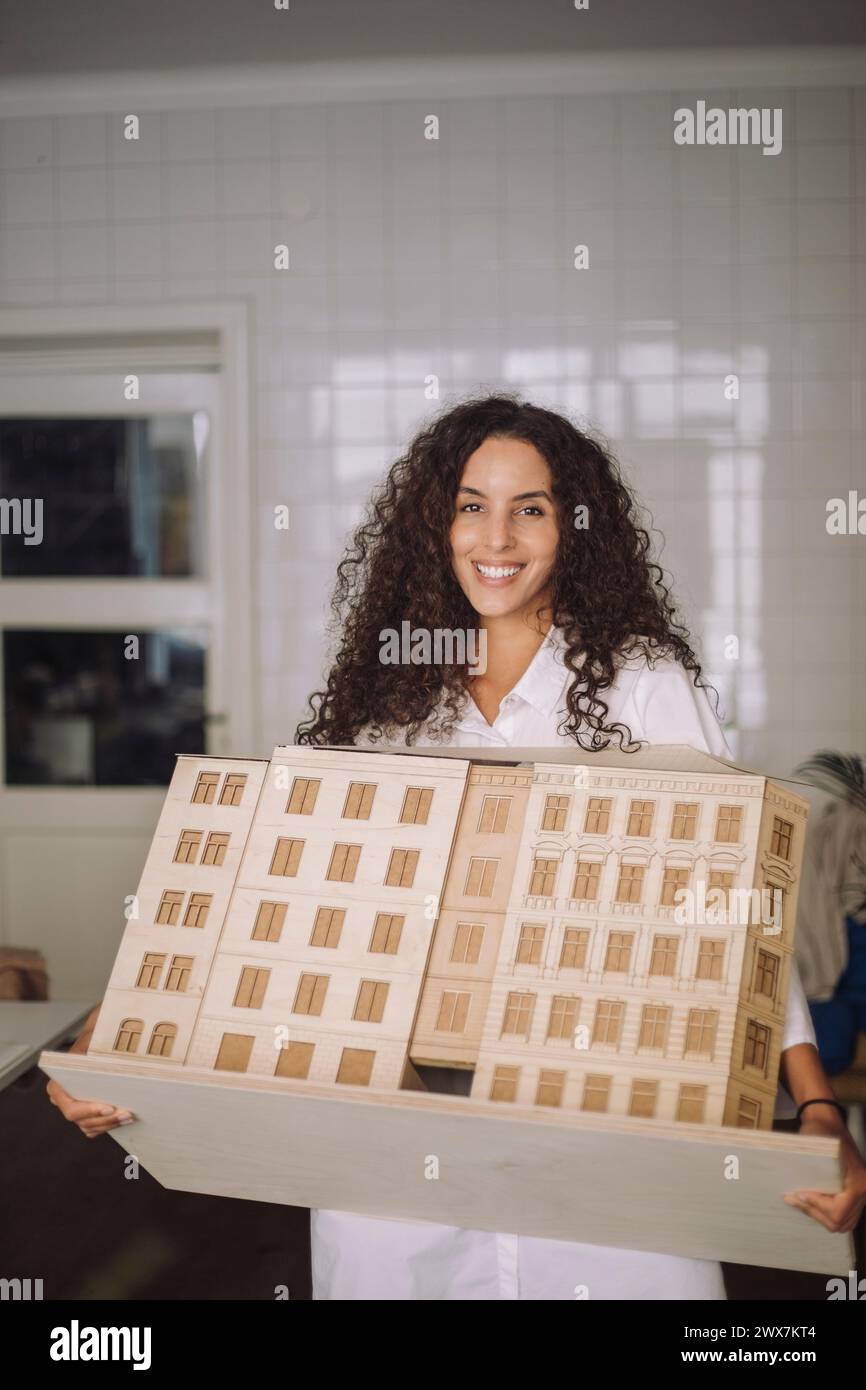 Ritratto di una donna sorridente architetto che tiene in mano il modello di edificio mentre si trova in ufficio Foto Stock
