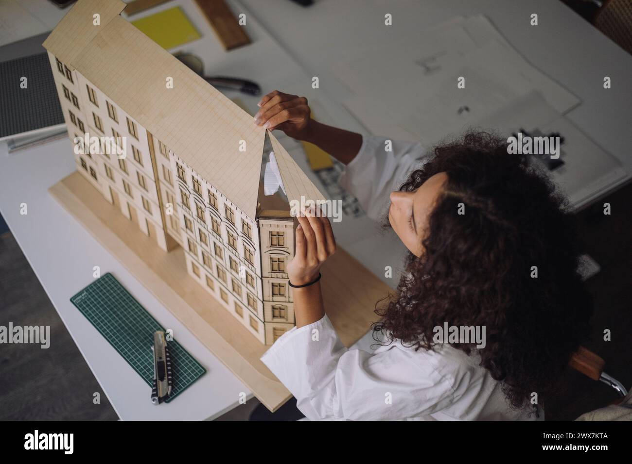 Vista ad angolo elevato della donna ingegnere edile che prepara il modello di edificio alla scrivania in ufficio Foto Stock
