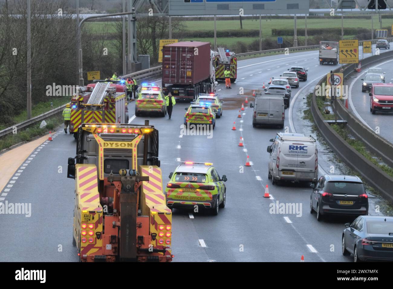 Bristol, Regno Unito. 28 marzo 2024. La pioggia e il vento ostacolano il recupero di un camion coinvolto in un incidente sulla Bristol M5 tra gli svincoli 15/16 e 17. La polizia, i vigili del fuoco e i veicoli adibiti al recupero stanno assistendo a un camion con danni frontali e segni di fuoriuscita di carburante sull'autostrada. Il traffico si muove lentamente in una corsia man mano che l'operazione procede, il che porta a un traffico molto lento per 16 miglia in corsa per la fuga di Pasqua. Crediti: JMF News/Alamy Live News Foto Stock