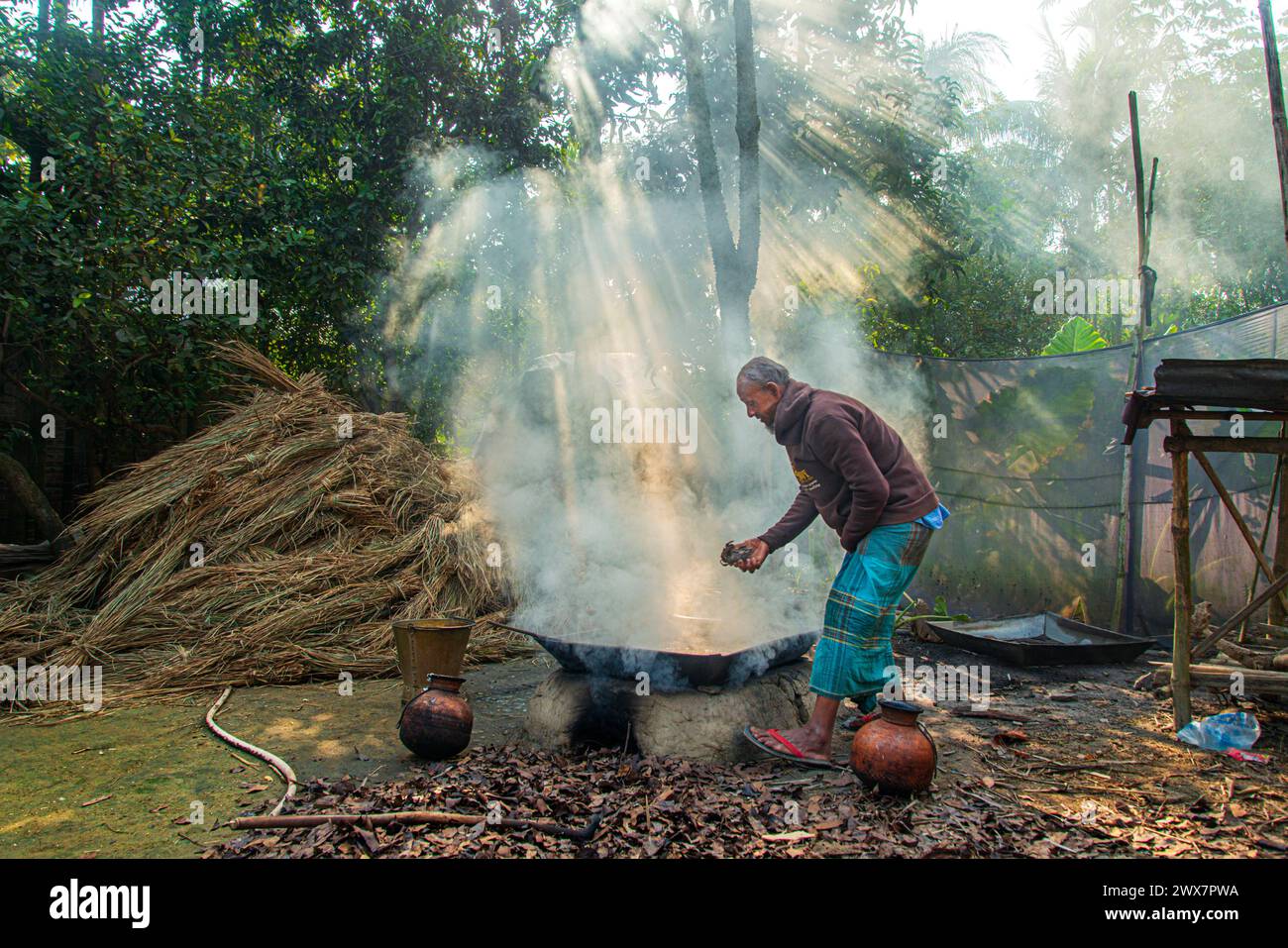 Un vecchio fa melassa bollendo il succo di dattero raccolto da palme da dattero in un grande vaso. In inverno, la linfa viene raccolta da palme e. Foto Stock