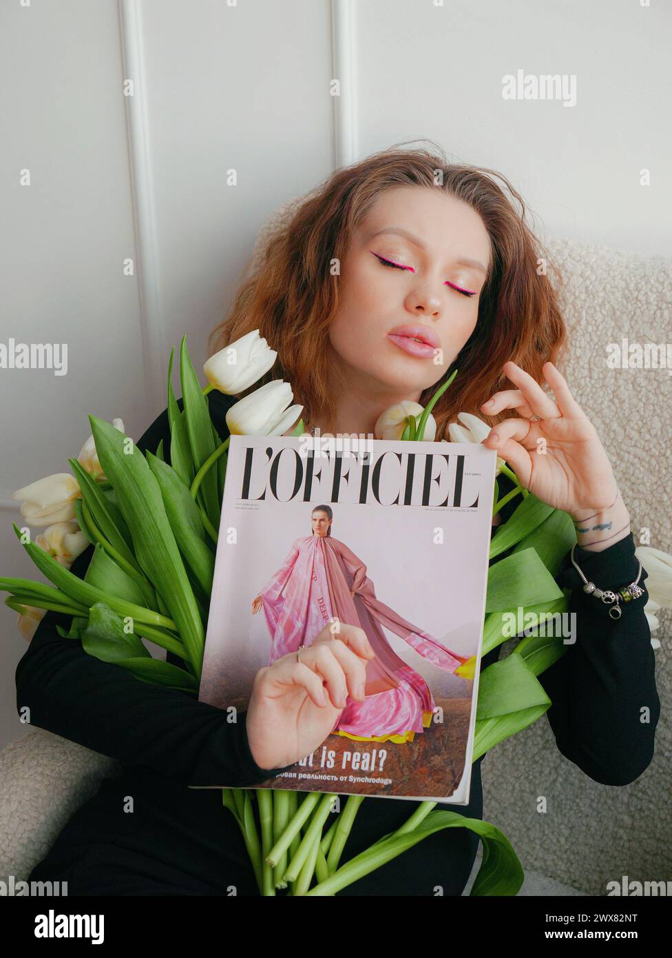 Una donna con un trucco a occhi rosa che indossa un abito stretto nero con tulipani bianchi Foto Stock