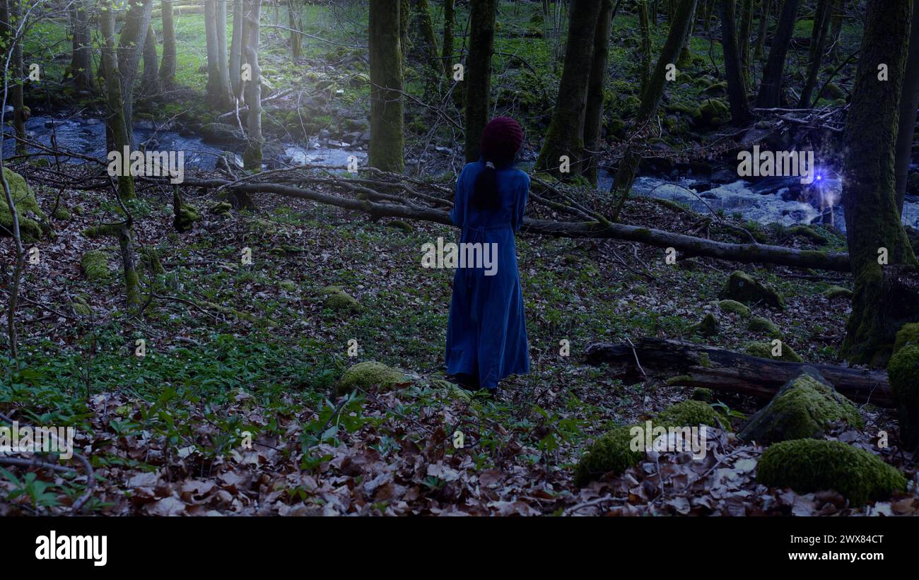 Donna che guarda una luce misteriosa nel bosco. Foto Stock