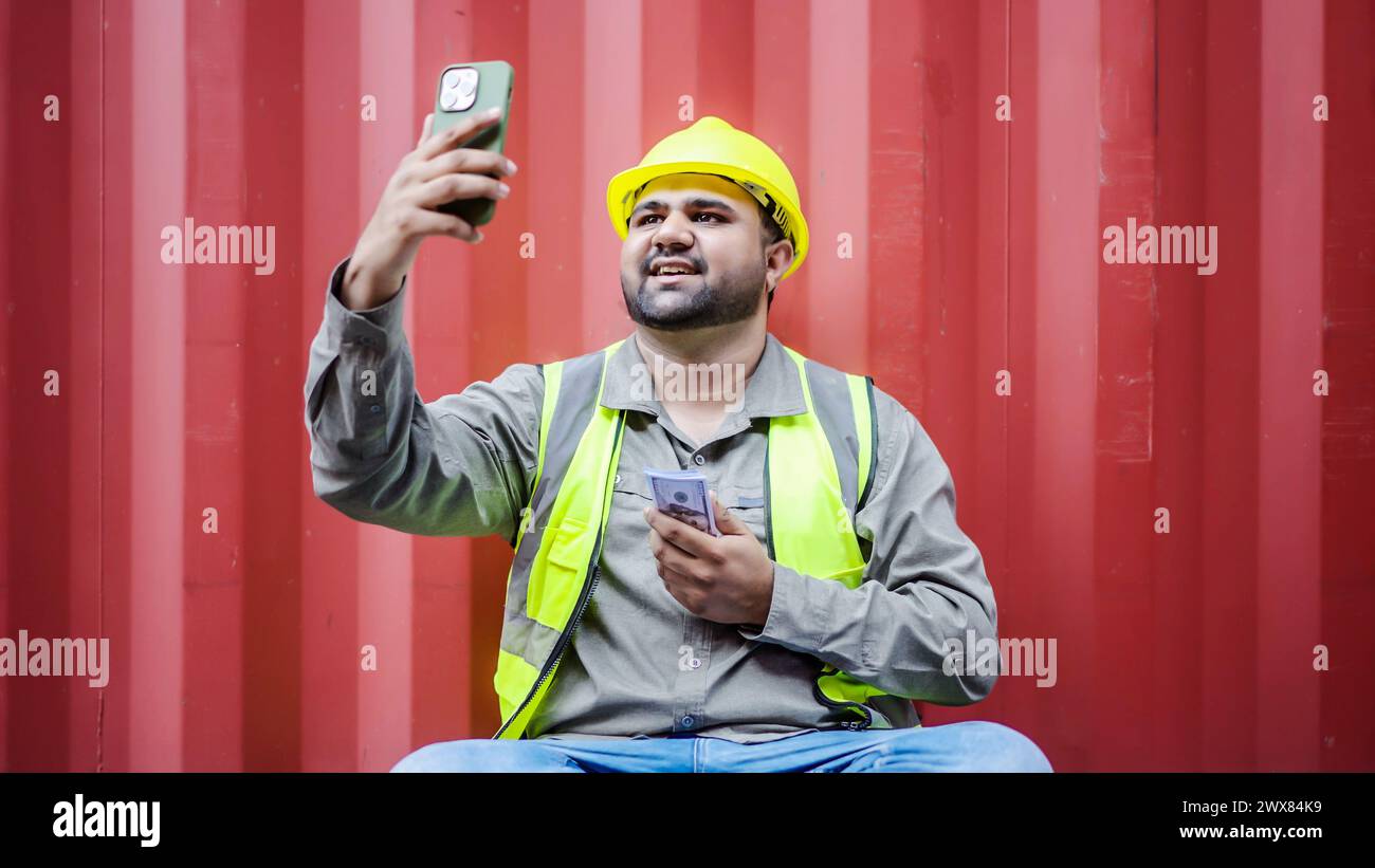 Uomo in gilet seduto sul marciapiede con il cellulare Foto Stock