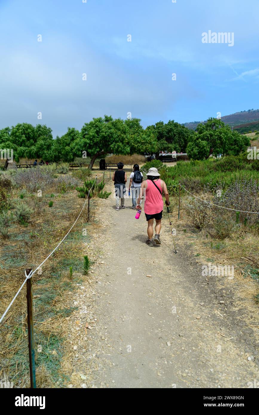 Tre persone camminano lungo il sentiero all'Abalone Cove Park a Rancho Palos Verdes, California, con alberi verdi in lontananza. Foto Stock