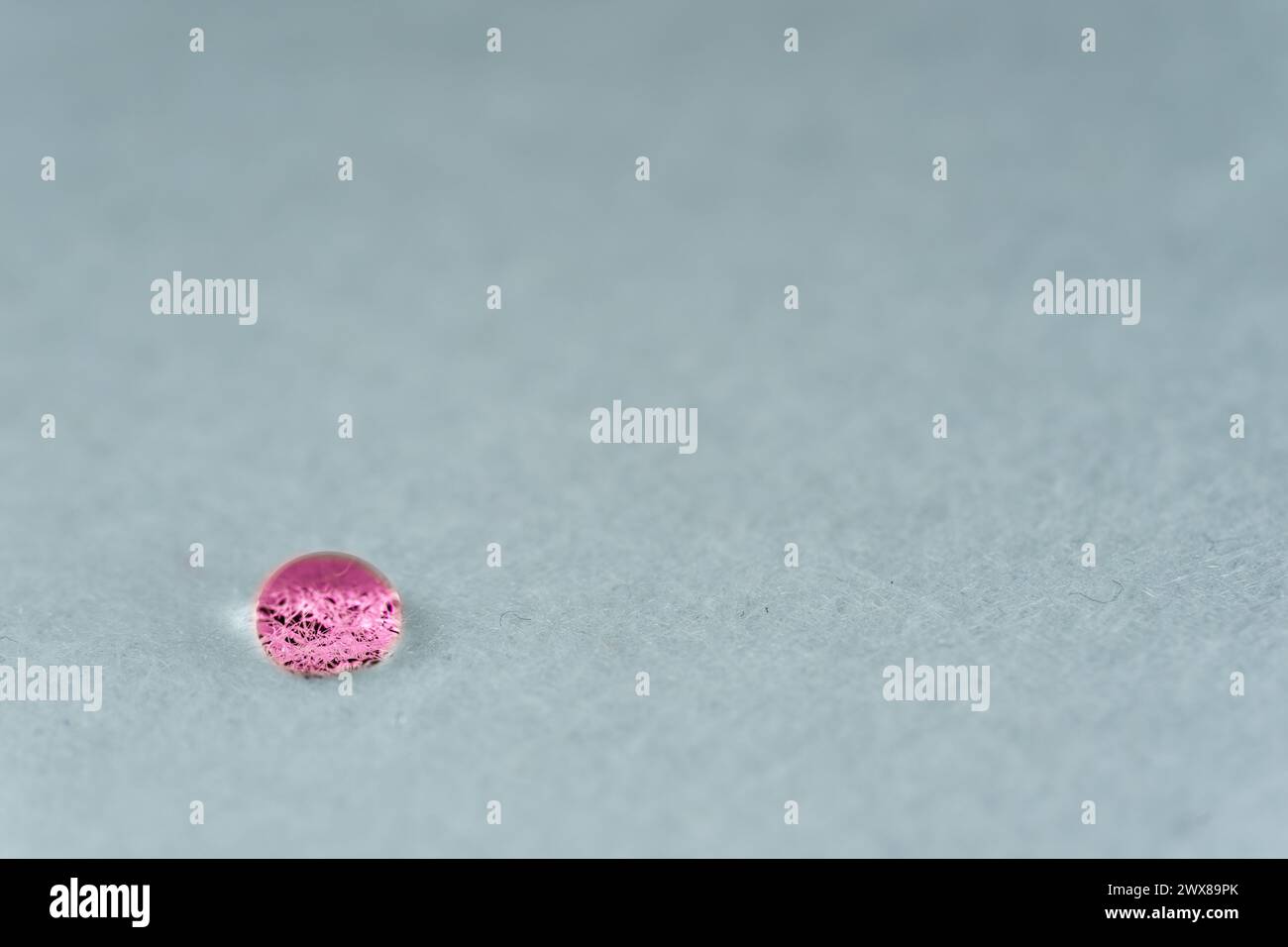 Goccia d'acqua rossa che sembra una pietra luminosa sopra un foglio di tessuto bianco. Foto Stock