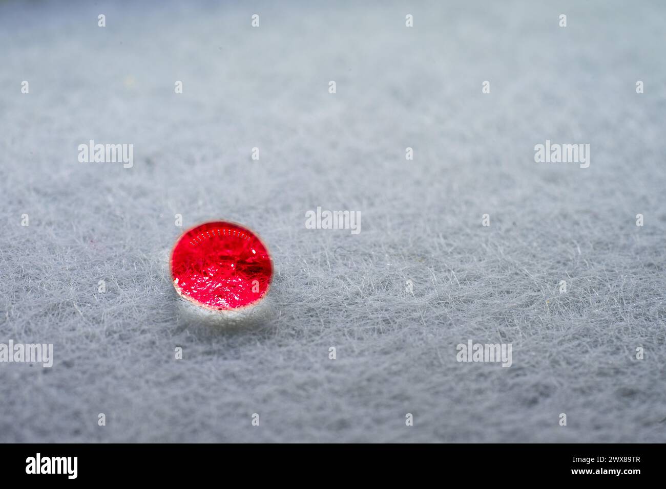 Goccia d'acqua rossa che sembra una pietra luminosa sopra un foglio di tessuto bianco. Foto Stock