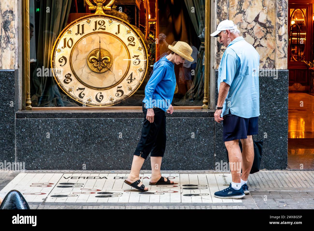 Due turisti che mettono i piedi sulle impronte di danza Tango fuori dalla Confiteria Ideal Cafe a Buenos Aires, Argentina. Foto Stock