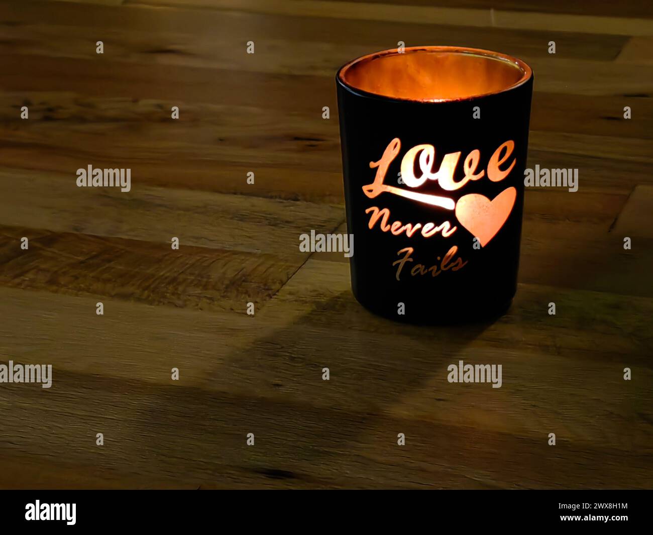 L'amore non fallisce mai. Vetro nero a lume di candela, messaggio. Su una superficie di legno marrone. Foto Stock