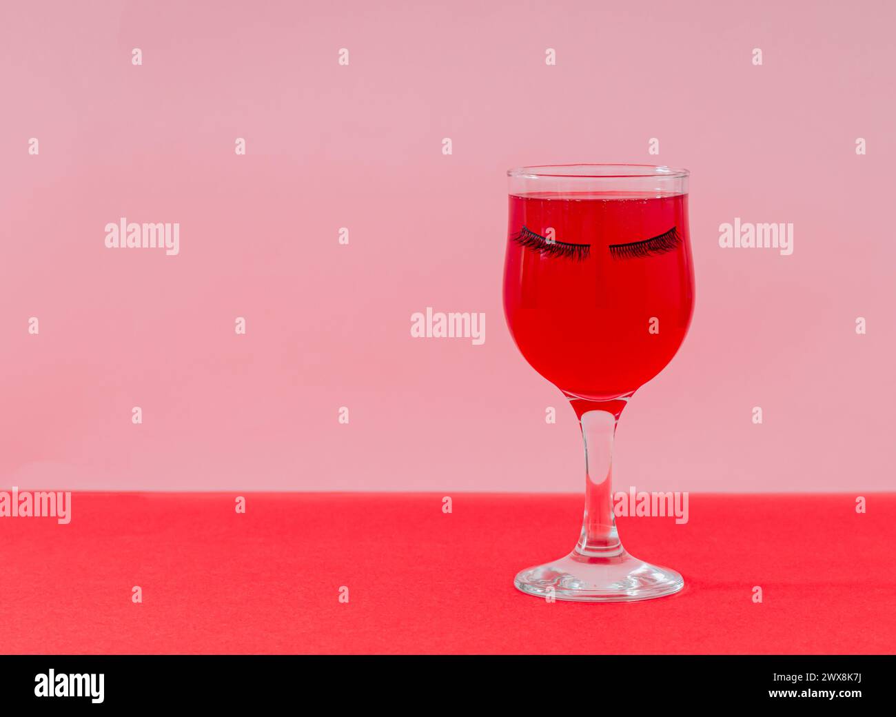 Layout creativo con bicchiere di vino rosso e ciglia finte su sfondo rosa e rosso. Moda bellezza composizione romantica. Festa dall'estetica retrò. Foto Stock