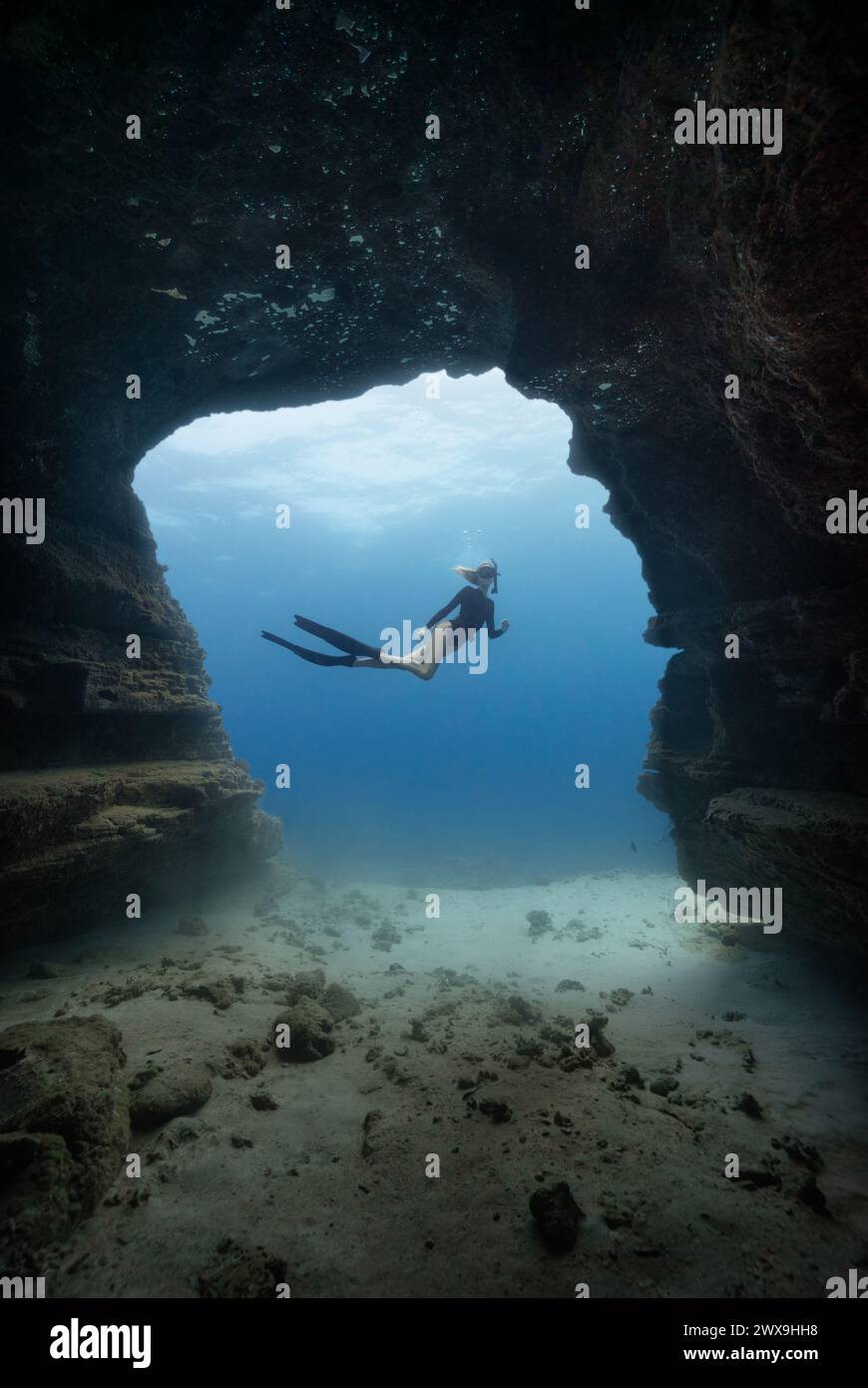 Una giovane femmina che si tuffa liberamente in una porta di una grotta nelle limpide acque blu delle Hawaii incorniciate da pareti ombrose della grotta. Rilascio modelli disponibile Foto Stock