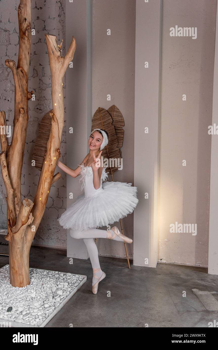Giovane ballerina in tutù bianco con un sorriso gioioso ingannato, cattura l'eccentricità della danza, circondata da arte rustica e da un soffice ed etereo giglio Foto Stock