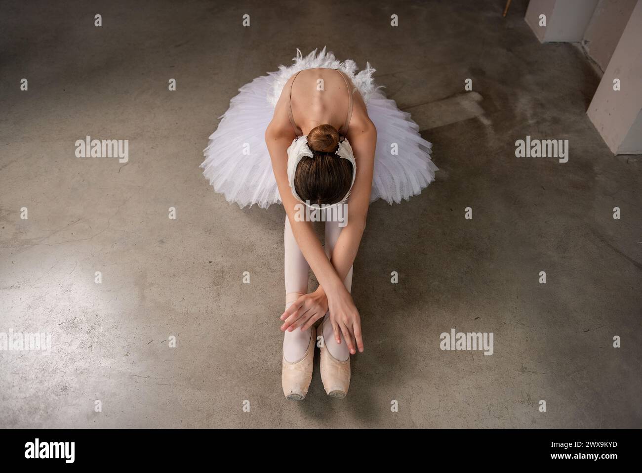 Giovane ballerina in balletto pointe, tutù bianco, tiara in sereno tratto, che si inchina in avanti seduto sul pavimento in contrasto con la morbidezza dell'abbigliamento. F Foto Stock