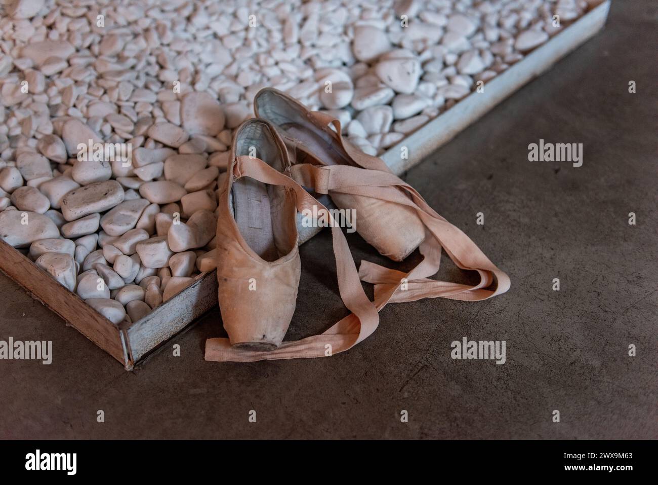 Un paio di ciabatte da balletto usate poggia su una superficie ricoperta di ciottoli, suggerendo la pratica rigorosa dietro il viaggio di un ballerino. Foto Stock