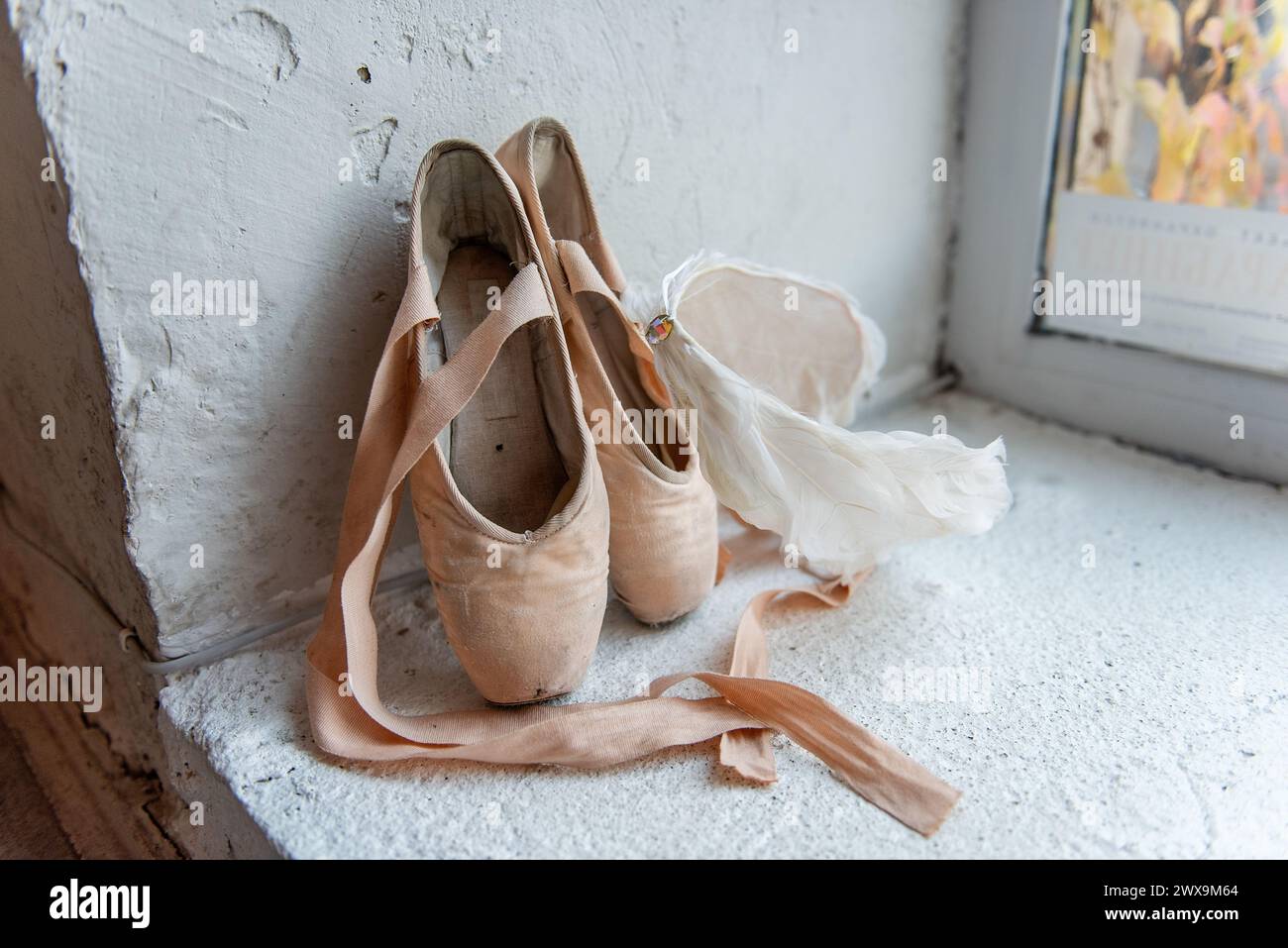 Scarpe pointe ben usate con nastri, tiara di piume bianche giacciono accanto alla finestra, raccontando la storia della dedizione e la graziosa arte del balletto. Foto Stock