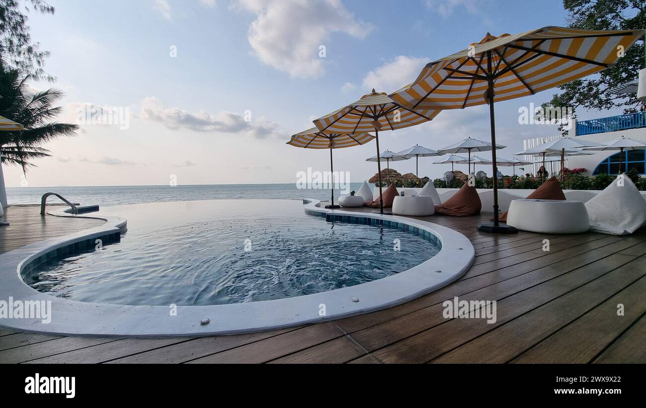 Bangsaray Pattaya Tailandia 28 febbraio 2024, Una lussuosa piscina in stile resort circondata da palme, affacciata su una spiaggia di sabbia incontaminata e sulle onde cristalline dell'oceano. Foto Stock
