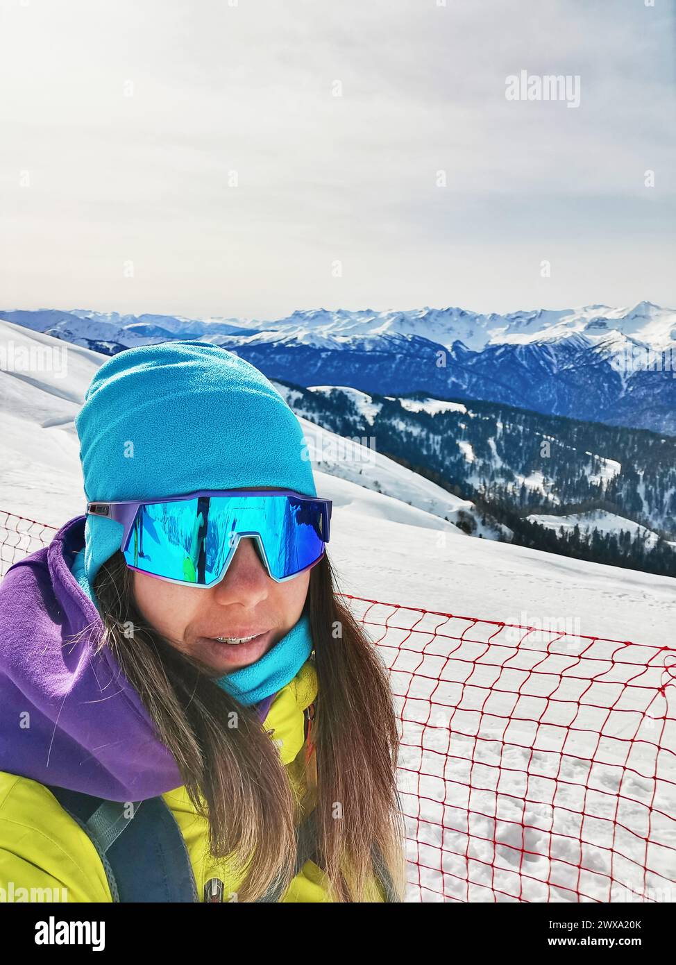 Uno sciatore alpino si fa un selfie con una vasta gamma di cime innevate alle sue spalle, con i suoi vibranti occhiali da sci che riflettono il sole invernale. Foto Stock