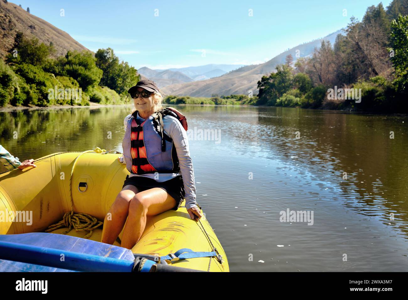 Donna anziana sorridente seduta su zattera gonfiabile che galleggia sul fiume Foto Stock