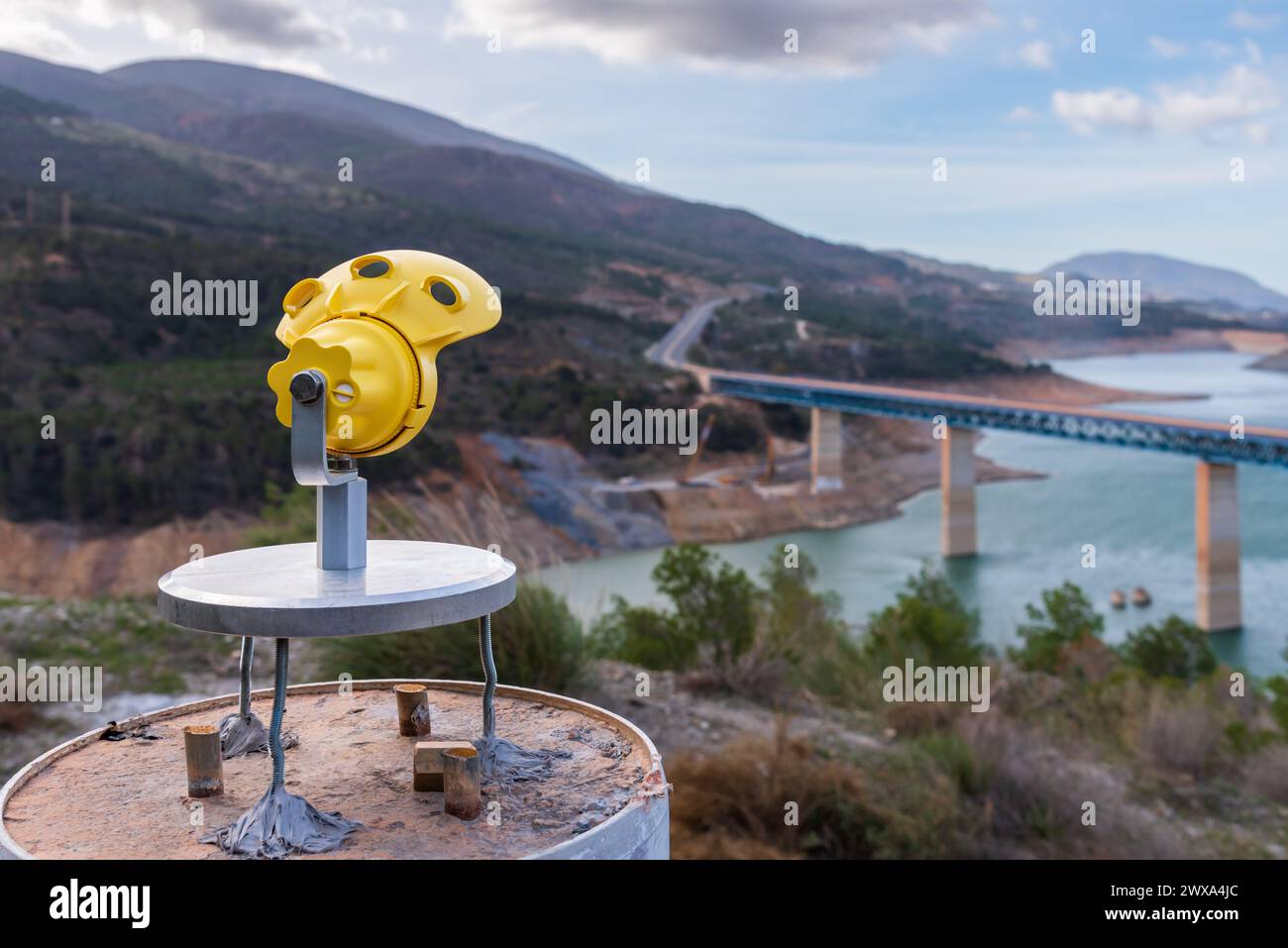 Mini prisma per l'uso nel rilevamento su un vertice fisso in cemento, sullo sfondo un ponte in riparazione da cui vengono monitorati i movimenti, vista posteriore. Foto Stock