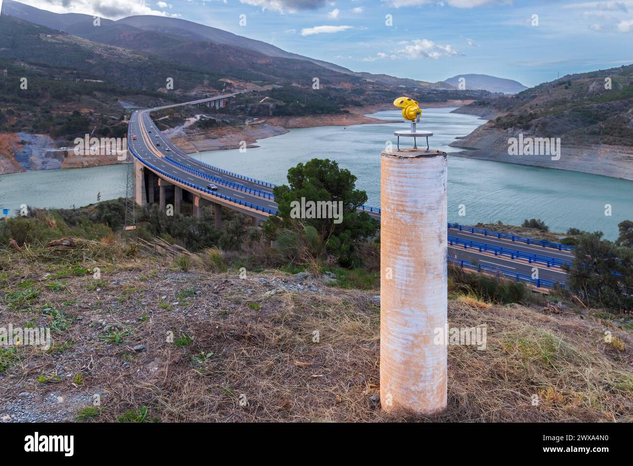 Mini prisma per l'uso in rilievo su un vertice fisso in cemento, sullo sfondo un ponte in riparazione da cui vengono monitorati i movimenti. Foto Stock