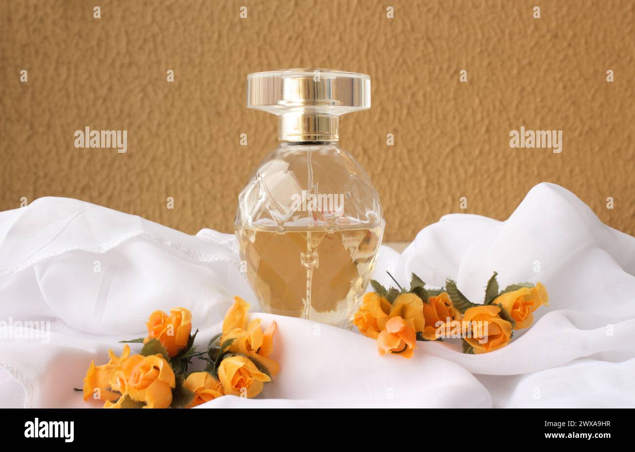 Profumo femminile su tessuto bianco con fiori di colore arancione davanti alla parete color senape. Eau de Parfum. Foto Stock