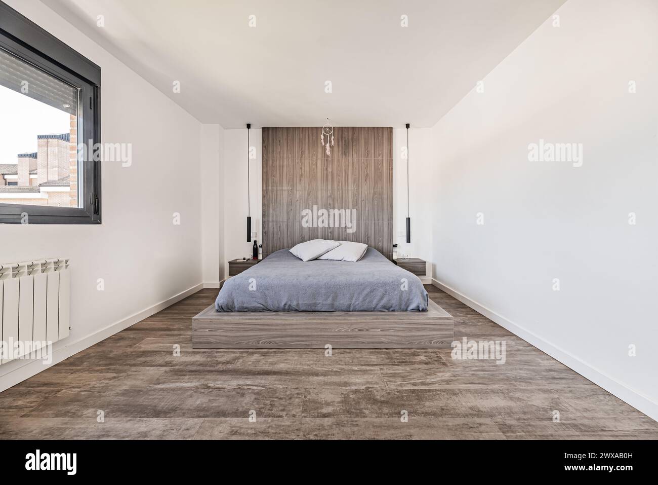 Grande testata in legno che si abbina al letto e al pavimento di una camera da letto con un grande letto con copriletto grigio Foto Stock