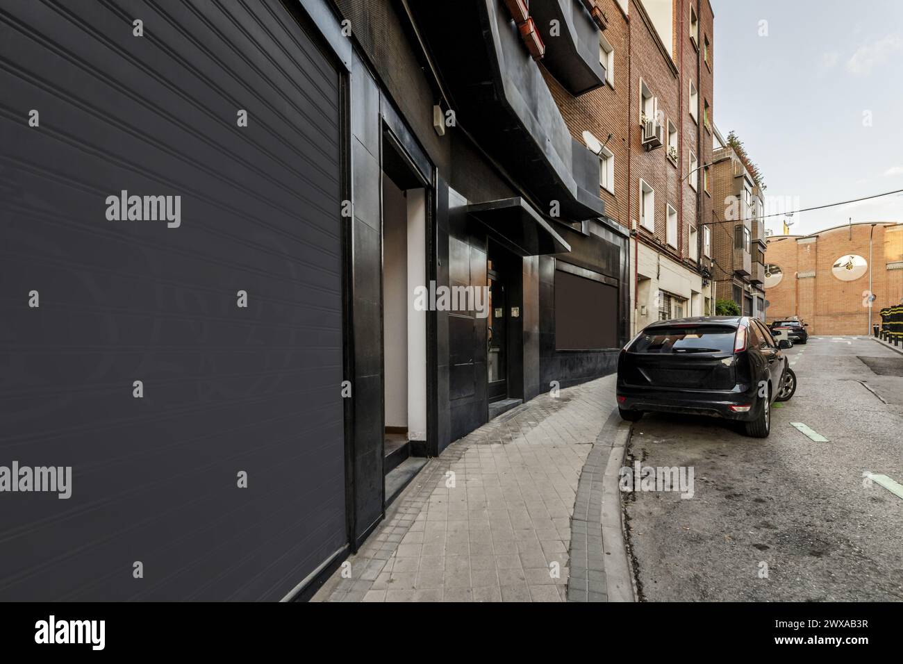 Locali commerciali con una facciata nera al piano terra di un edificio con veicoli parcheggiati sulla strada Foto Stock