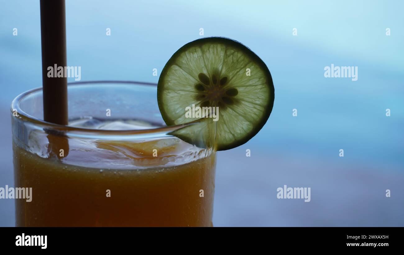 Succo di mango in un alto vetro trasparente con cuneo di lime per la decorazione e paglia di legno con sfondo blu Foto Stock