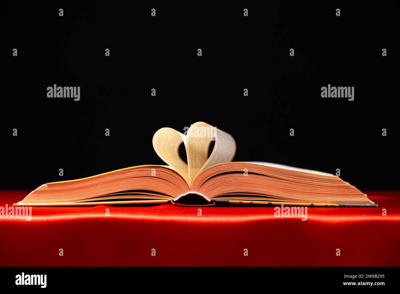 Le pagine del libro sono piegate a forma di cuore su uno sfondo rosso e nero, posto per il testo. Foto Stock