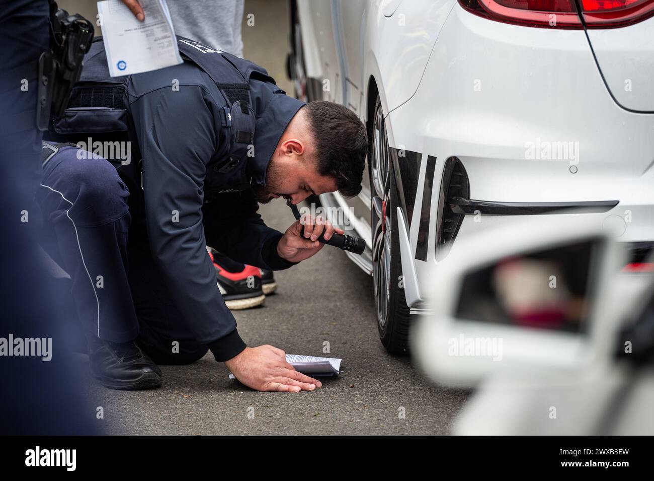 Bochum, Germania. 29 marzo 2024. Un agente di polizia controlla un veicolo in un parcheggio il "venerdì dell'auto". La polizia aveva istituito un posto di blocco di fronte al Ruhr Park per dare un'occhiata più da vicino alle auto convertite. Crediti: Christian Knieps/dpa/Alamy Live News Foto Stock