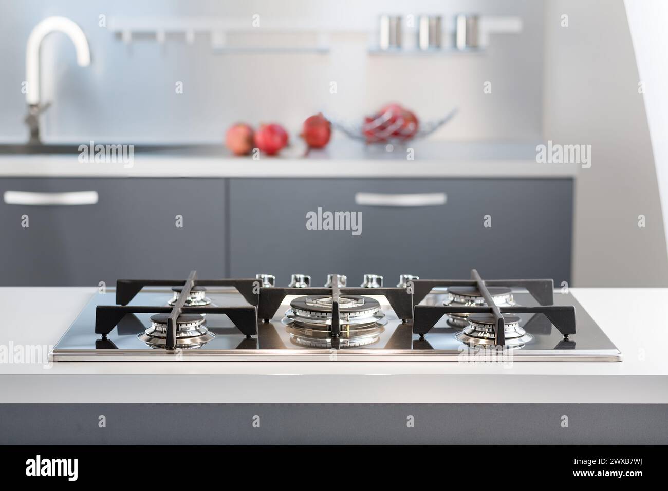 Elegante cucina casalinga con piano cottura in acciaio inox, piano di appoggio bianco e mele rosse. Il design minimalista incontra la funzionalità e lo stile contemporaneo. Foto Stock