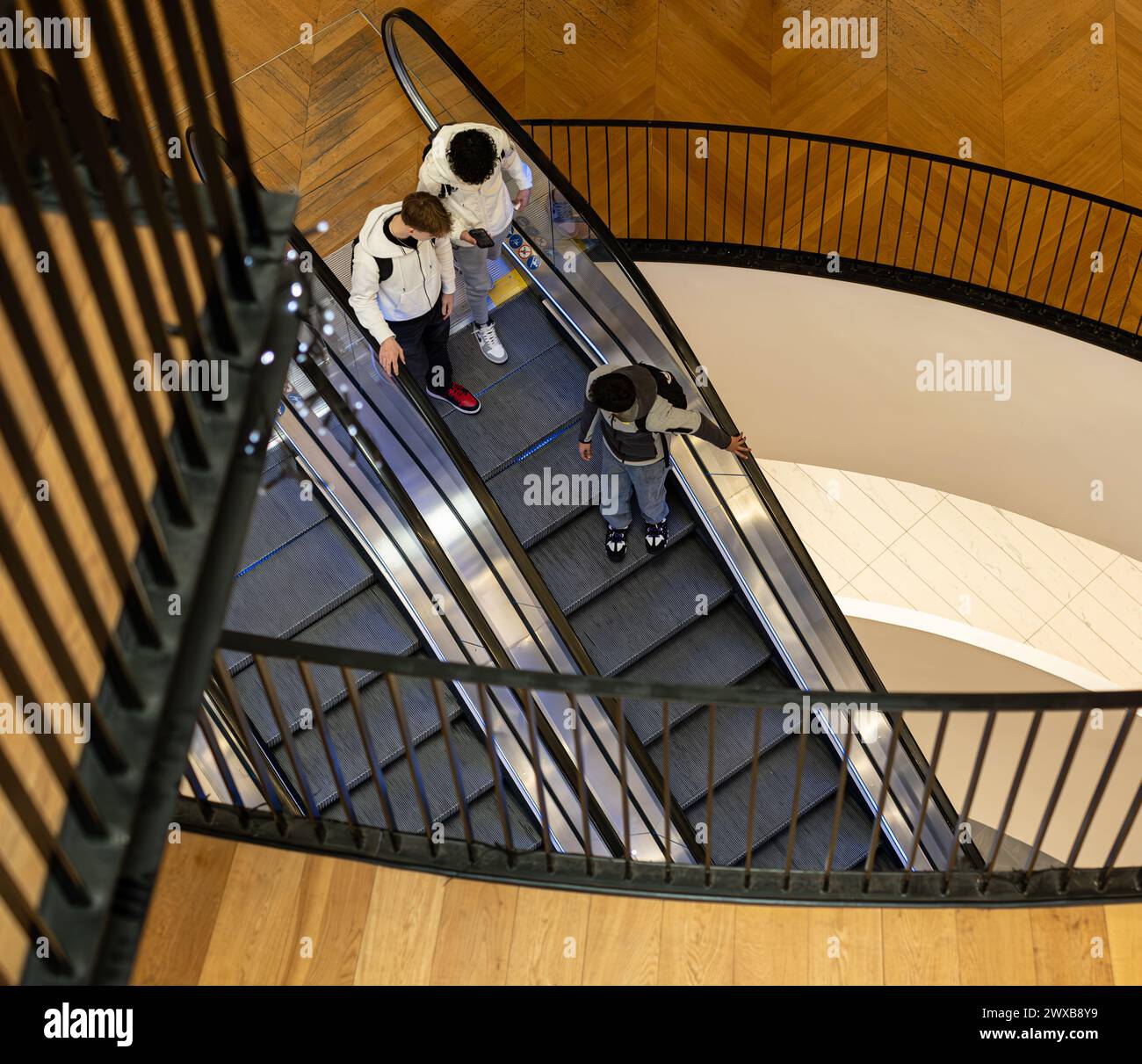 Vista dall'alto di tre giovani uomini su una scala mobile nella Birmingham City Library a più piani. Ringhiere della galleria a diversi livelli e vista attraverso. Foto Stock