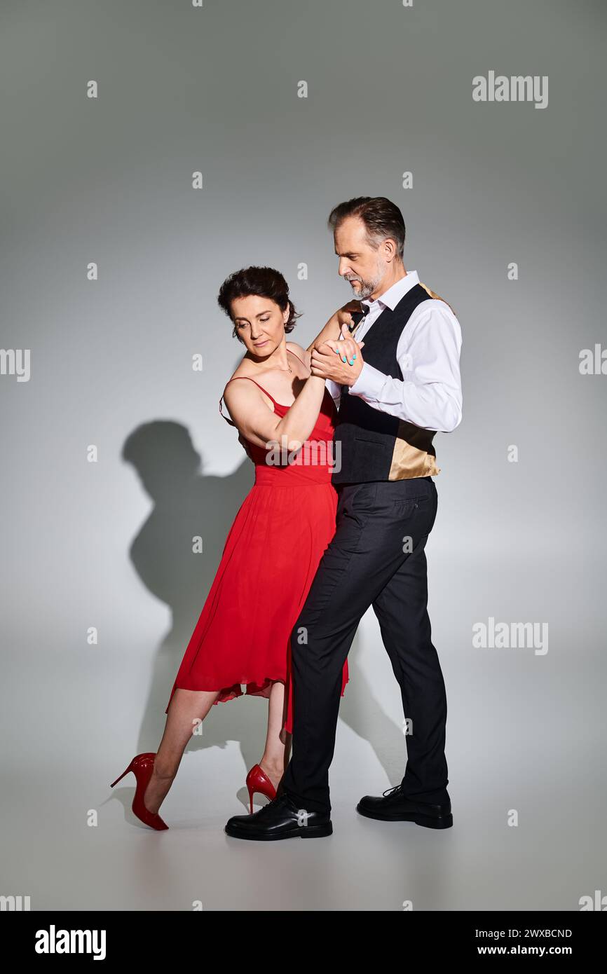 Sala da ballo per coppie di mezza età con abito rosso e abito da ballo con tango isolato su sfondo grigio Foto Stock