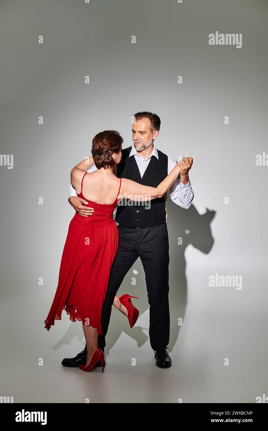 Immagine di una coppia matura di ballerini di tango in abito rosso e vestito che si esibiscono su sfondo grigio Foto Stock
