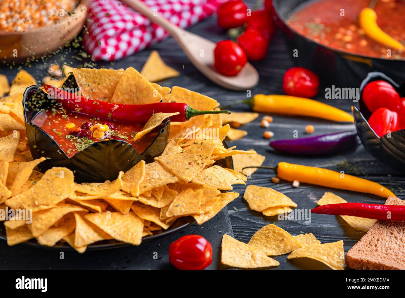 Il prezzemolo cade in una ciotola di peperoncino con carne, circondata da tortilla chips, pomodori, chicchi di mais e peperoni Foto Stock
