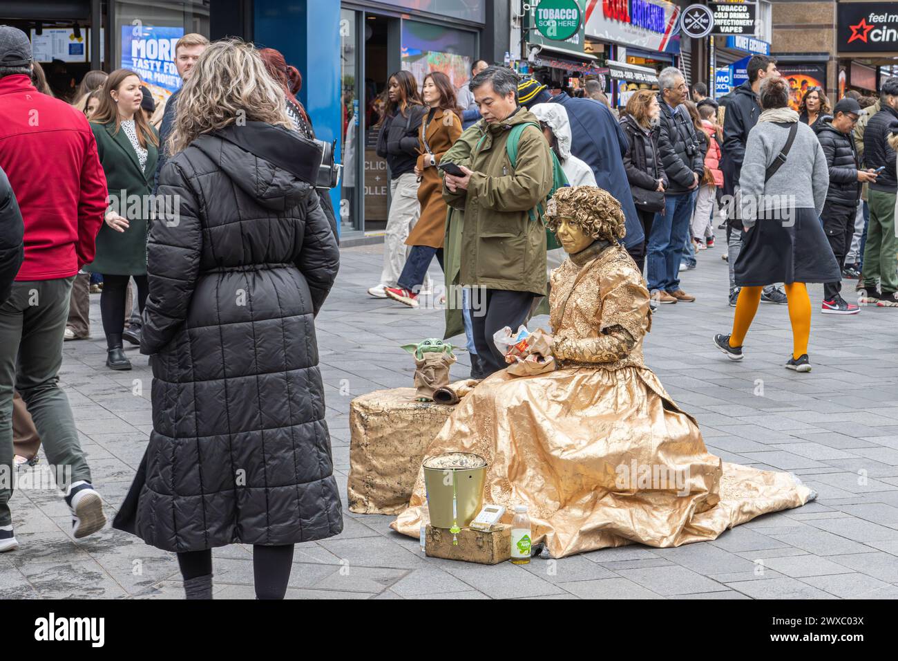 Una statua vivente femminile o umana fa una pausa per pranzare mentre la gente guarda. Un artista di strada guarda il mondo passare mentre pranza Foto Stock