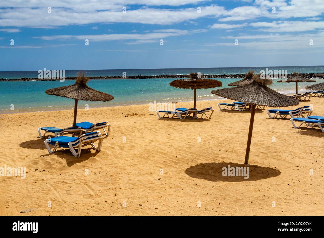 Una spiaggia vuota in bassa stagione con ombrelloni di paglia e sdraio blu. Playa del Castillo , Fuerteventura, Isole Canarie, Spagna Foto Stock