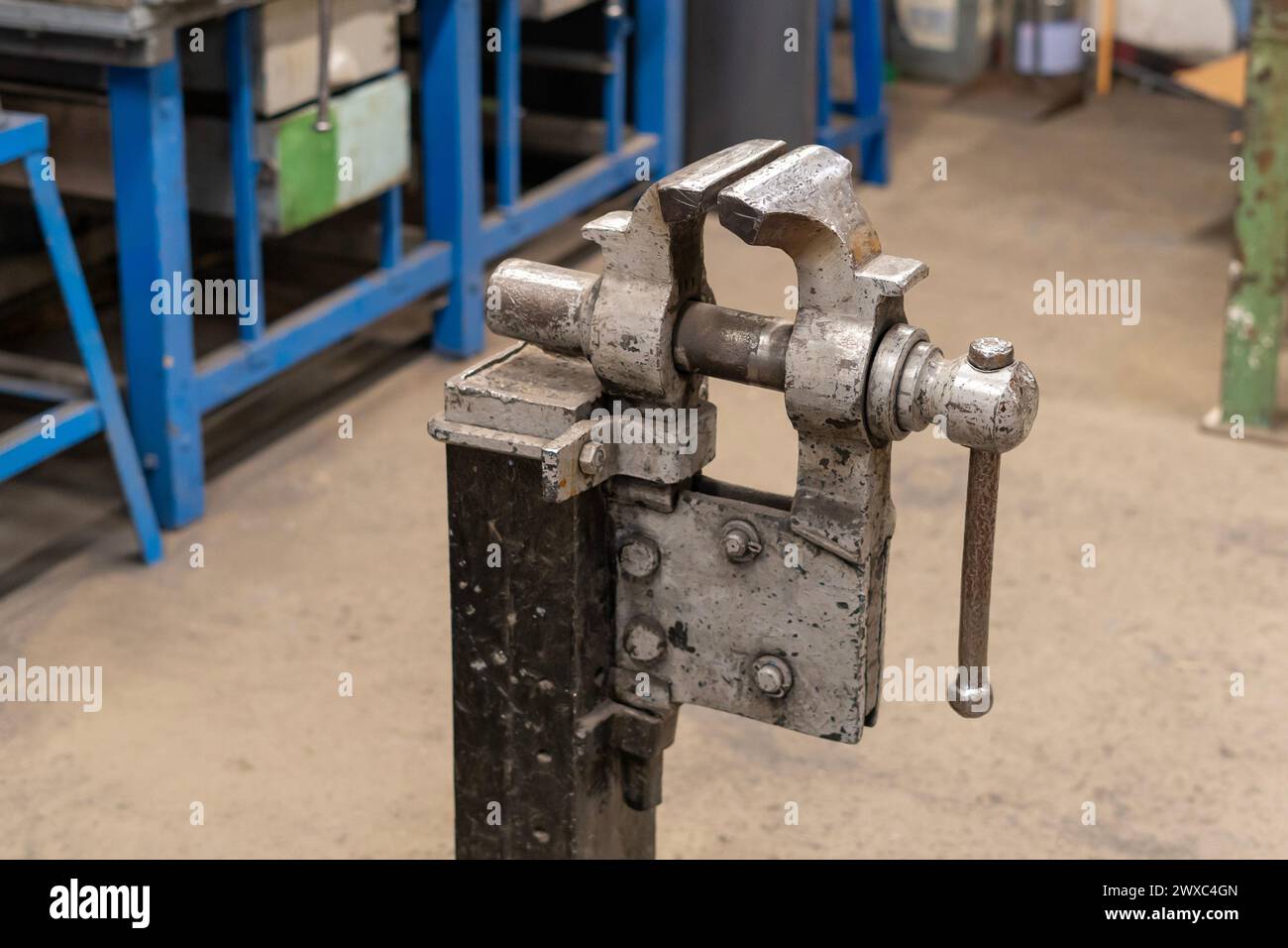 Una morsa vecchia, usurata e verniciata in grigio su un supporto al centro di un'officina di saldatura vuota Foto Stock