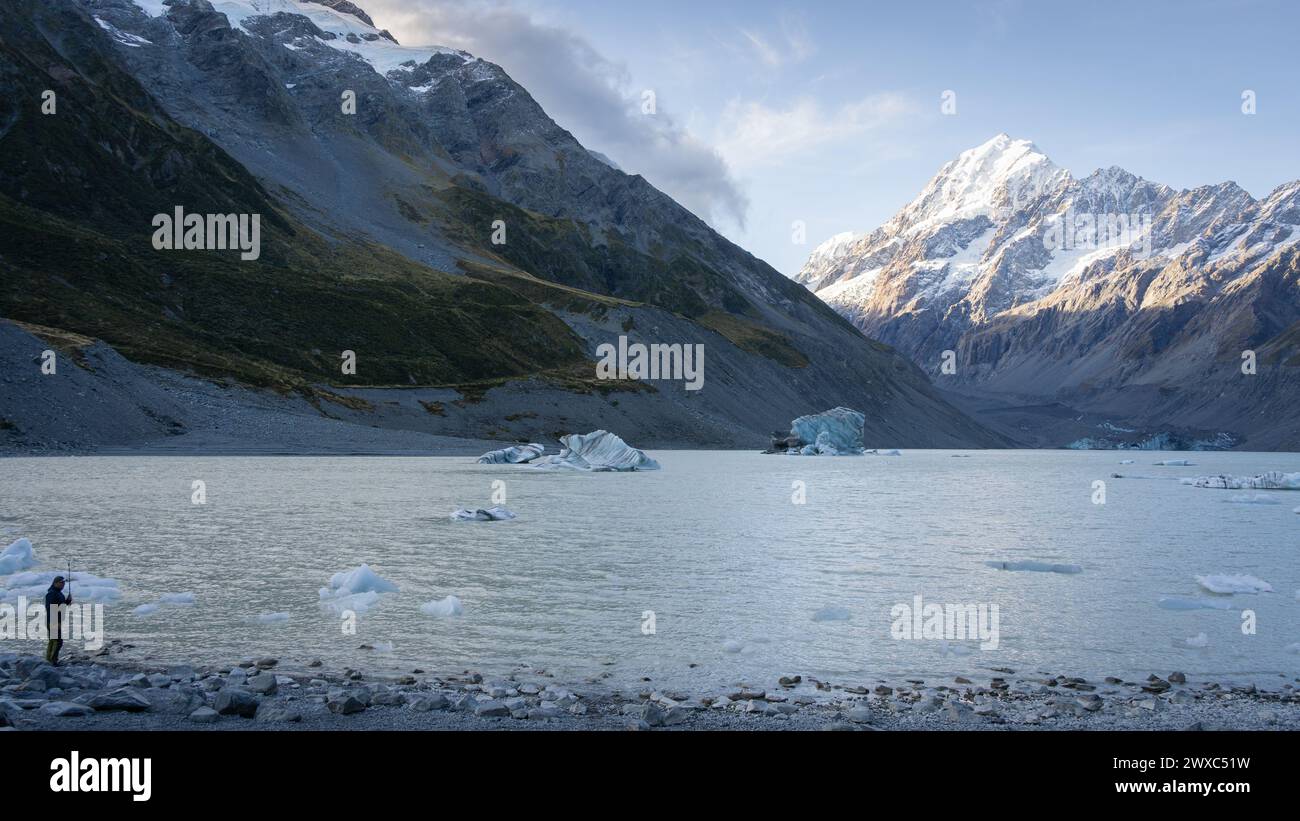 Uomo in piedi sulla riva del lago glaciale alpino con ghiacciaio e massiccia montagna innevata sullo sfondo. Foto Stock