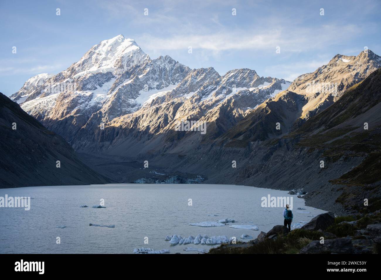 Donna in piedi in un bellissimo paesaggio con ghiacciaio, lago glaciale e enorme montagna innevata, nuova Zelanda. Foto Stock