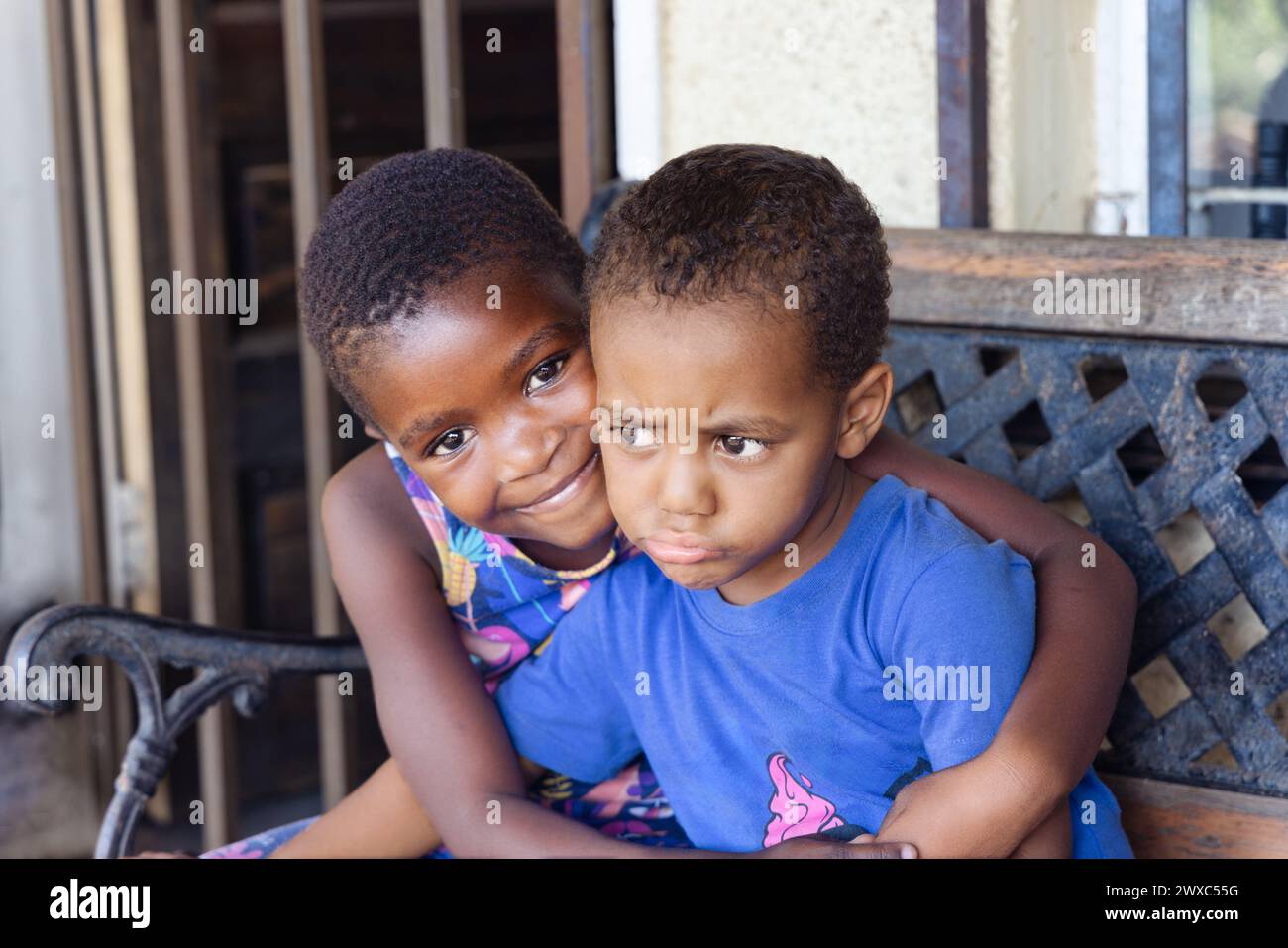 bambini africani seduti di fronte alla casa su una panchina, porta con sbarre di ladro in un insediamento informale Foto Stock