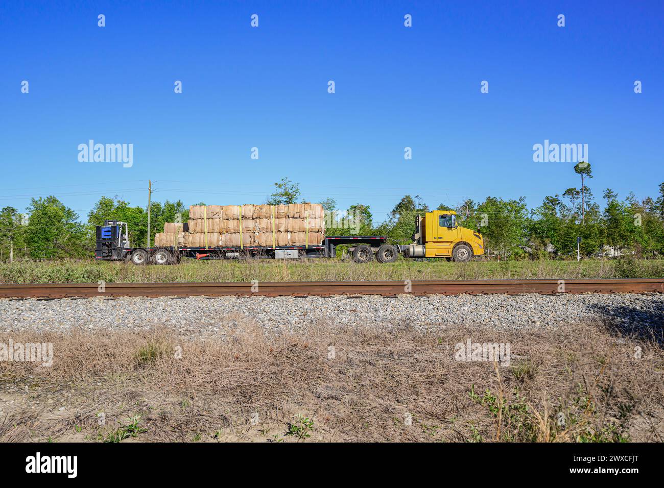 "Sostenibilità di rotolamento: Un trattore-rimorchio che trasporta cartone riciclato, con la sua cabina gialla che guida la carica, viaggia lungo l'autostrada, emblematico o Foto Stock
