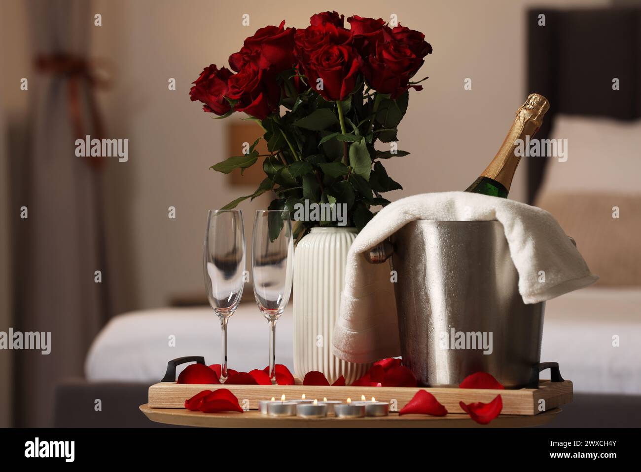 Luna di miele. Vino frizzante, bicchieri e bouquet di rose su un tavolo di legno in camera Foto Stock