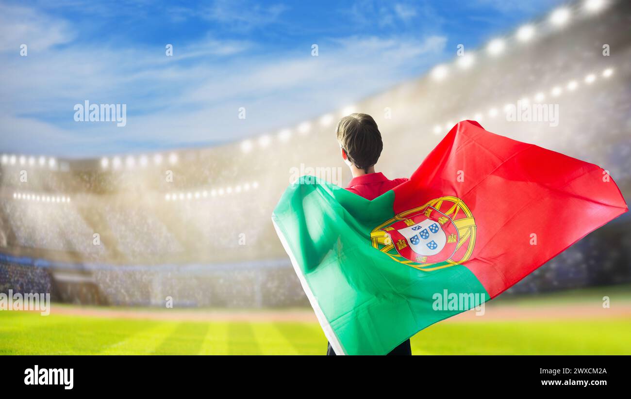 Sostenitore di football portoghese allo stadio. Tifosi portoghesi sul campo di calcio che guardano la squadra giocare. Gruppo di tifosi con bandiera e maglia nazionale di coraggio Foto Stock