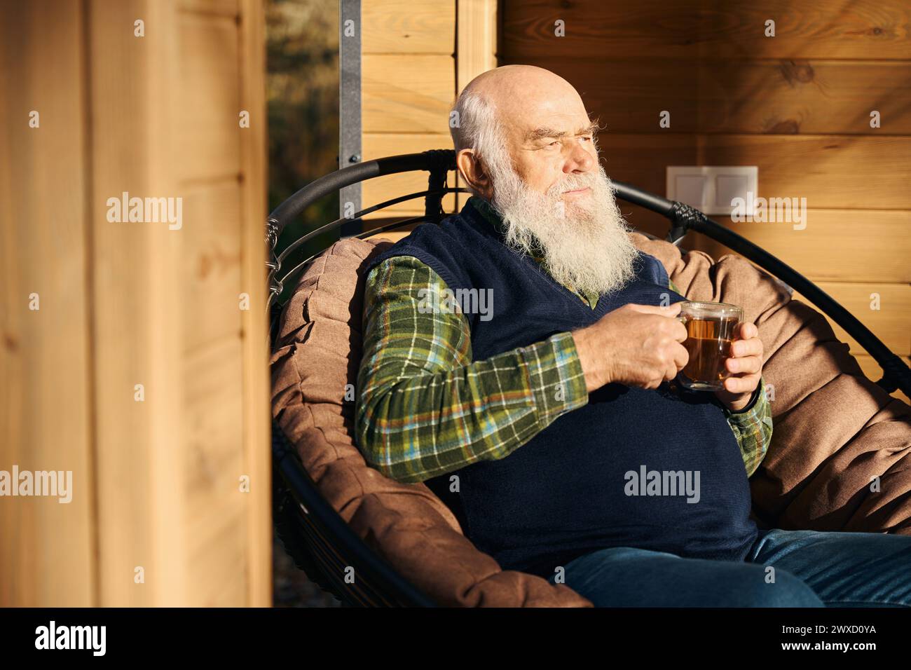 Il vecchio barbuto si trova sulla veranda con una tazza di tè Foto Stock