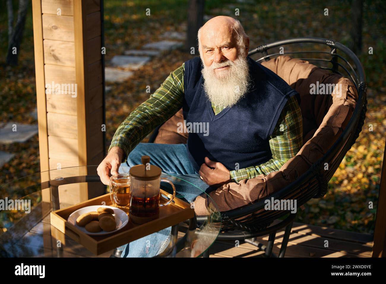 Il vecchio con la barba grigia sta bevendo il tè sulla veranda Foto Stock