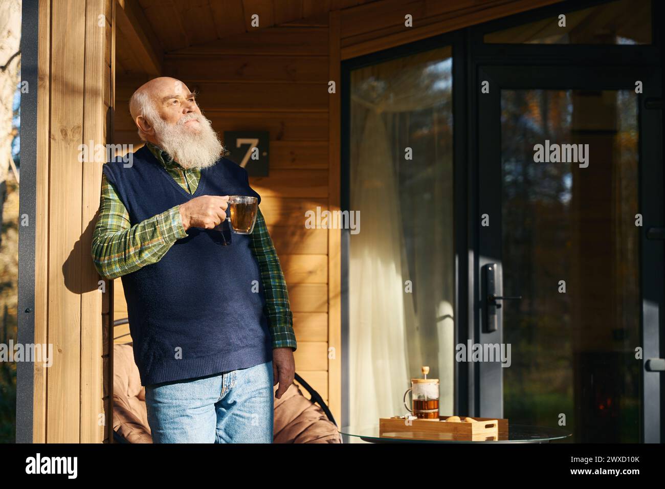 Un anziano uomo dai capelli grigi si gode una tazza di tè in veranda Foto Stock
