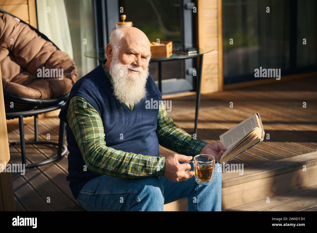 Vecchio carino seduto con un libro sul portico Foto Stock